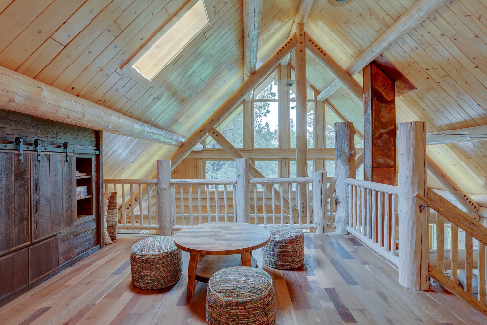 Inspiration for a large rustic mezzanine games room in Other with brown walls, medium hardwood flooring, a built-in media unit, brown floors, a reading nook, a two-sided fireplace and a stone fireplace surround.