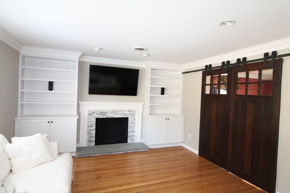 This is an example of a medium sized classic enclosed games room in Philadelphia with grey walls, medium hardwood flooring, a standard fireplace, a stone fireplace surround, a wall mounted tv and brown floors.