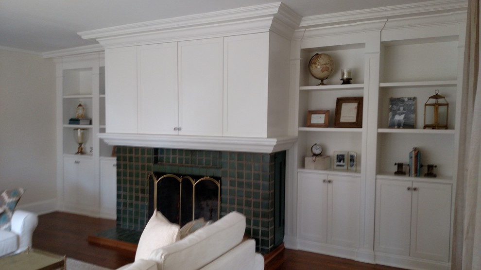 Modelo de sala de estar clásica con paredes blancas, suelo de madera en tonos medios, todas las chimeneas, marco de chimenea de baldosas y/o azulejos y televisor retractable