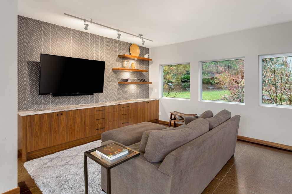 Diseño de sala de estar con biblioteca abierta contemporánea de tamaño medio sin chimenea con paredes grises, suelo de cemento y televisor colgado en la pared