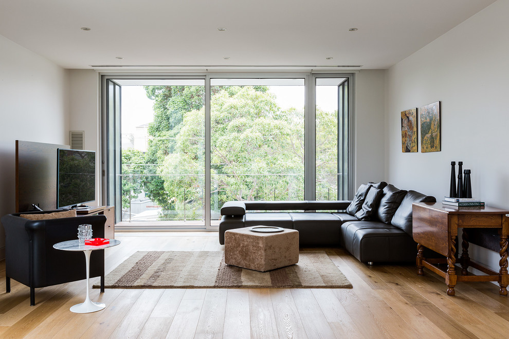 Modelo de sala de estar actual con paredes blancas, suelo de madera en tonos medios y televisor independiente