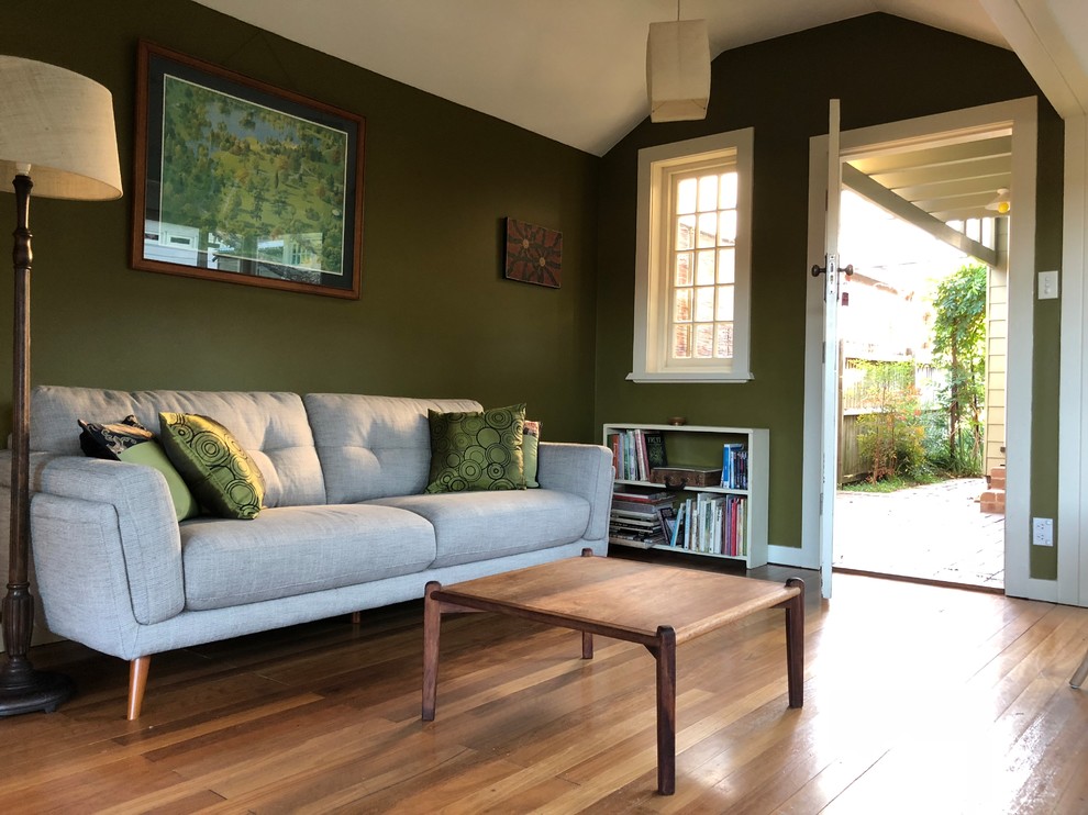 Réalisation d'une salle de séjour craftsman de taille moyenne et fermée avec un mur vert, un sol en bois brun, aucune cheminée, un téléviseur d'angle et un sol marron.