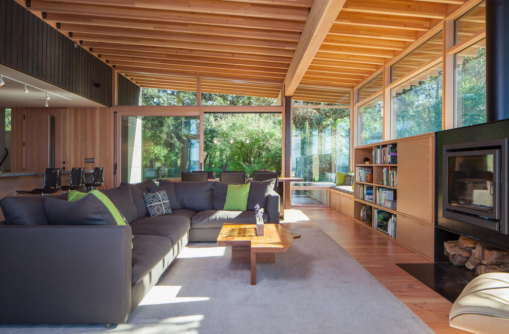 Aménagement d'une salle de séjour contemporaine ouverte avec un sol en bois brun, une cheminée standard, une bibliothèque ou un coin lecture, un manteau de cheminée en métal, un téléviseur dissimulé et canapé noir.