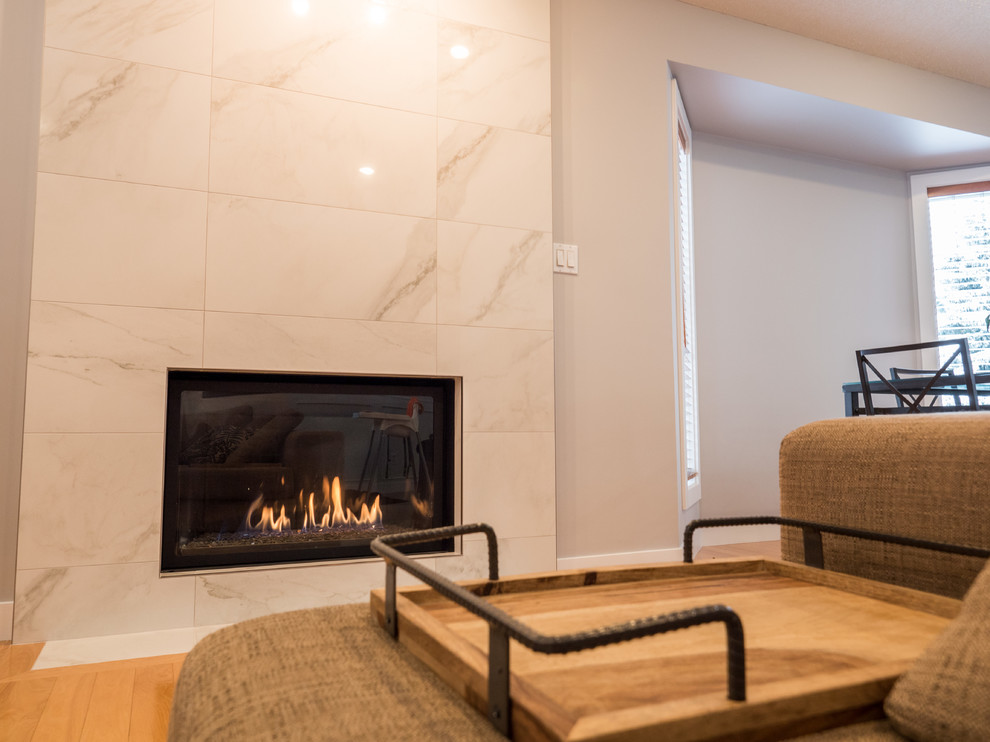 エドモントンにある中くらいなコンテンポラリースタイルのおしゃれなオープンリビング (グレーの壁、淡色無垢フローリング、標準型暖炉、テレビなし、ベージュの床、タイルの暖炉まわり) の写真