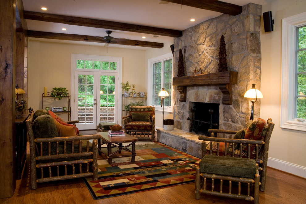 Imagen de sala de estar abierta rural de tamaño medio sin televisor con paredes beige, suelo de madera en tonos medios, todas las chimeneas, marco de chimenea de piedra y suelo marrón