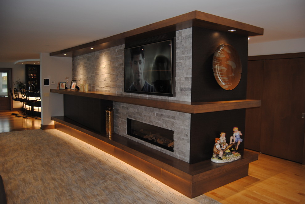 Modern inredning av ett mellanstort allrum med öppen planlösning, med en hemmabar, ljust trägolv, en bred öppen spis, en spiselkrans i sten, en väggmonterad TV, grå väggar och brunt golv