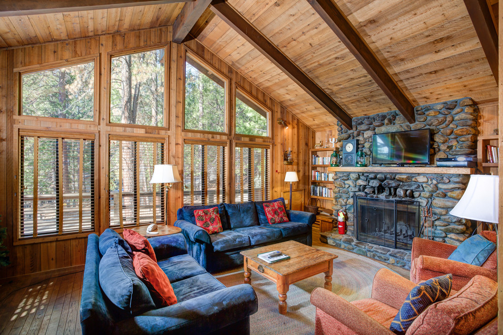Imagen de sala de estar con biblioteca rústica con suelo de madera en tonos medios, todas las chimeneas y marco de chimenea de piedra