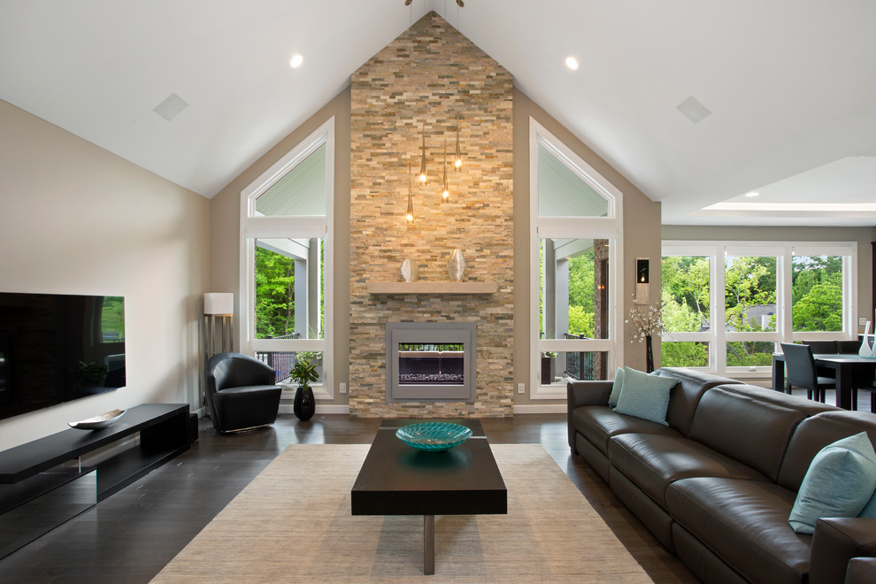 Diseño de sala de estar moderna grande con paredes grises, chimenea de doble cara y marco de chimenea de piedra
