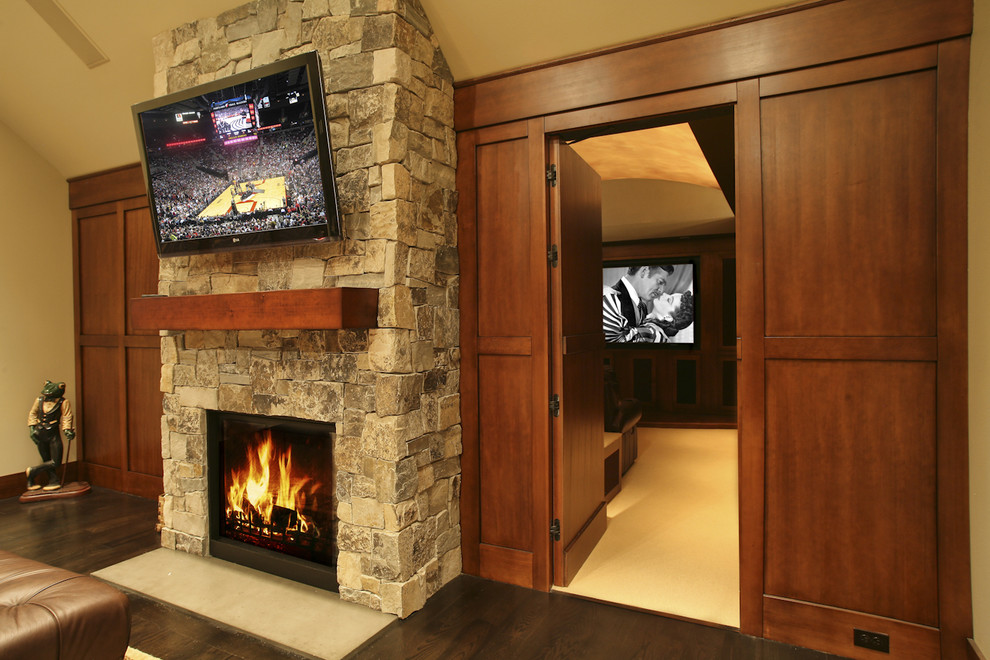 Imagen de sala de estar con barra de bar cerrada clásica grande con televisor colgado en la pared, suelo de madera oscura, todas las chimeneas y marco de chimenea de piedra