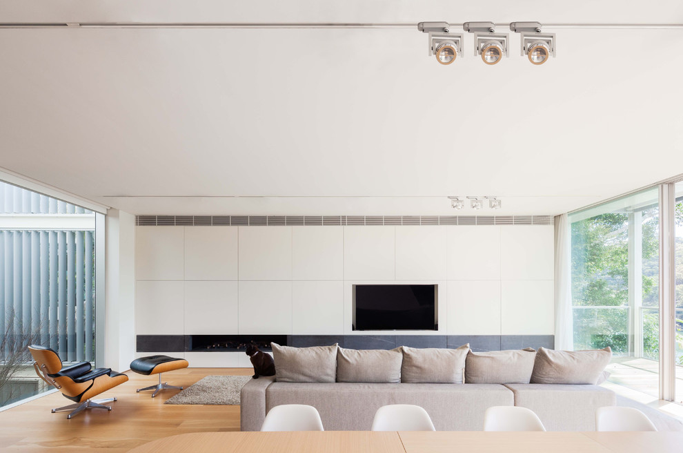 Modelo de sala de estar abierta minimalista con paredes blancas, suelo de madera en tonos medios, chimenea lineal, marco de chimenea de piedra, pared multimedia y suelo marrón