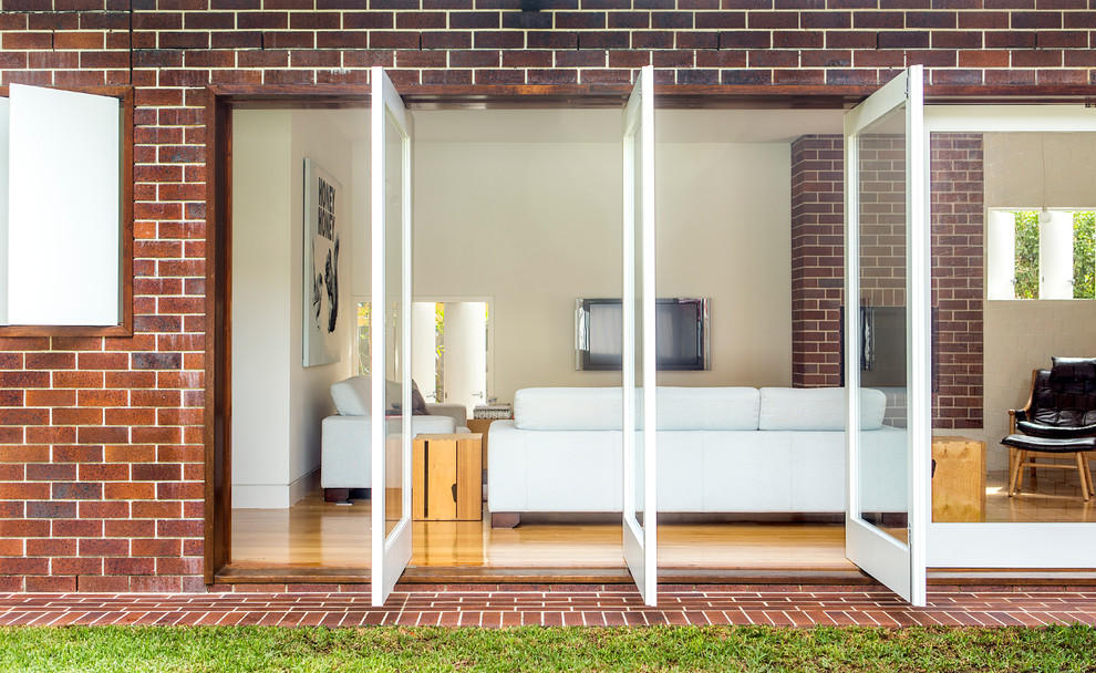 Offenes Modernes Wohnzimmer mit beiger Wandfarbe, braunem Holzboden, TV-Wand und Kaminumrandung aus Backstein in Brisbane