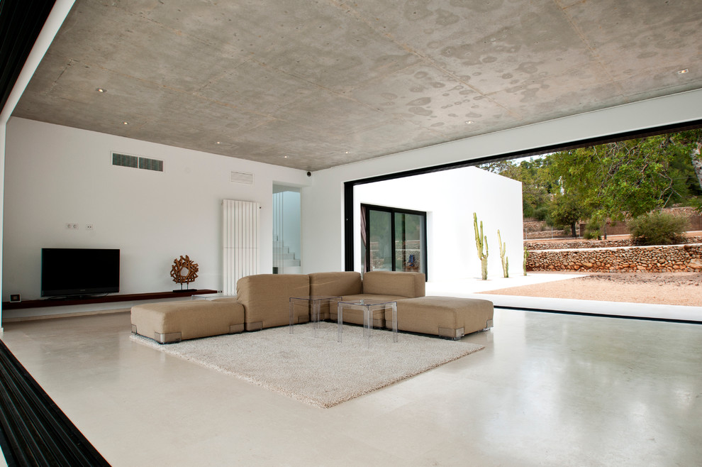 Modelo de sala de estar abierta mediterránea grande sin chimenea con paredes blancas, suelo de cemento y televisor independiente