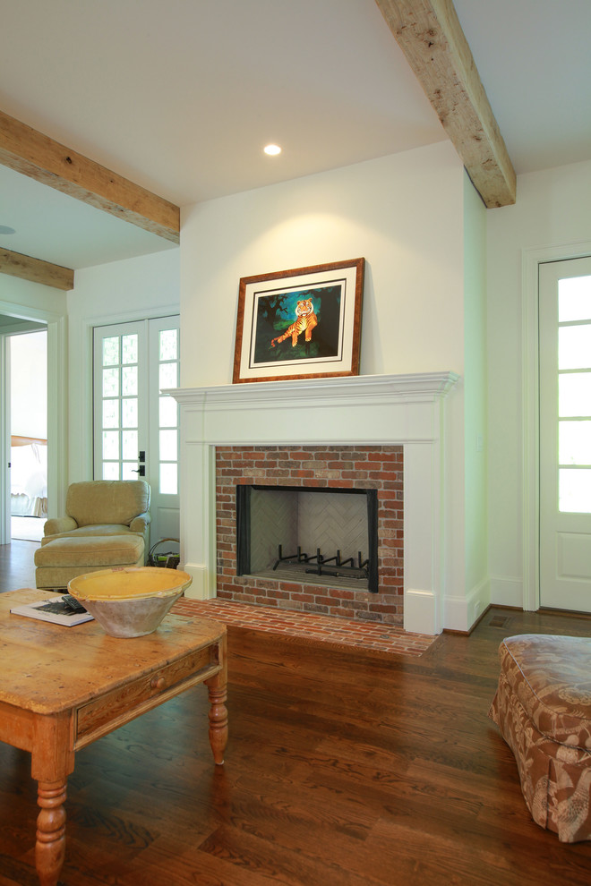 Cette photo montre une salle de séjour chic ouverte avec un mur blanc, un sol en bois brun, une cheminée standard et un manteau de cheminée en brique.