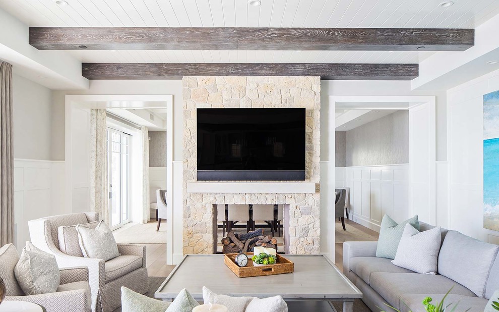 Свежая идея для дизайна: гостиная комната в морском стиле с серыми стенами, двусторонним камином, фасадом камина из камня и телевизором на стене - отличное фото интерьера