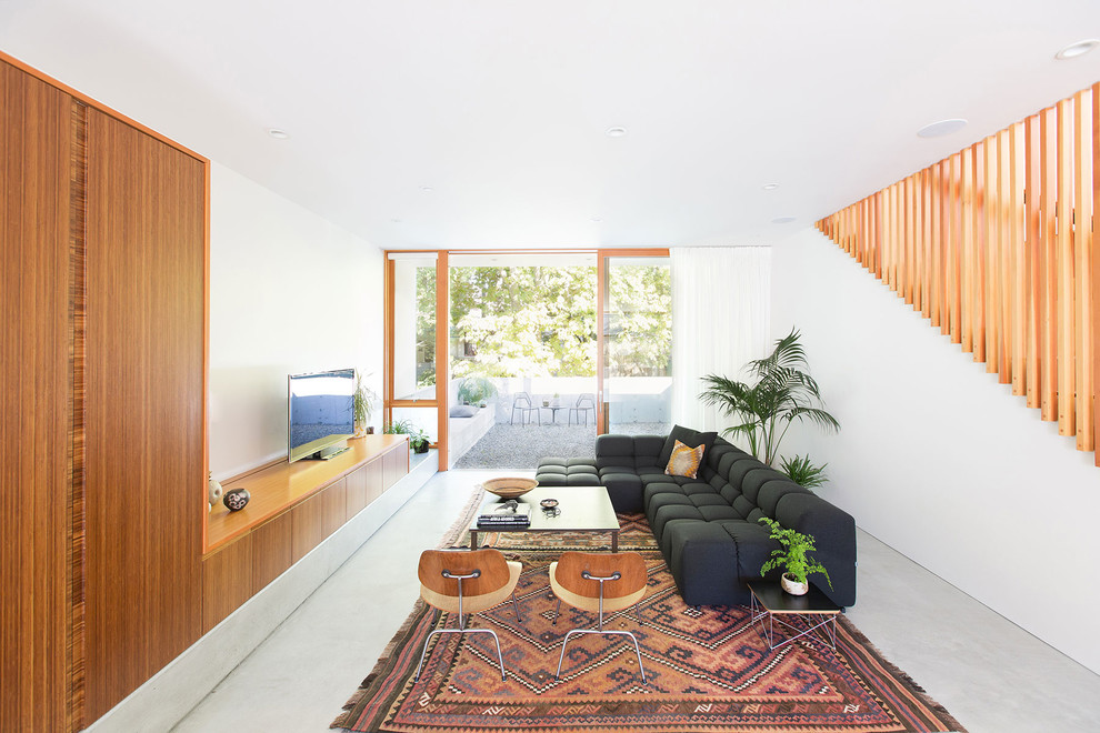 Diseño de sala de estar contemporánea con paredes blancas, suelo de cemento, televisor independiente y suelo gris