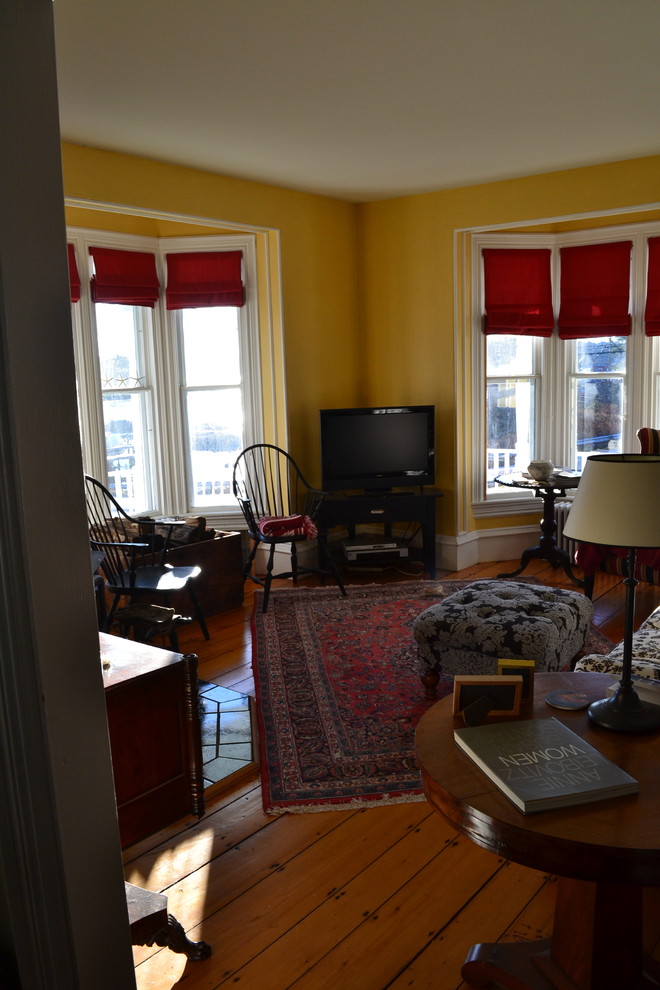 This is an example of a medium sized classic enclosed games room in Portland Maine with yellow walls, dark hardwood flooring, a freestanding tv, a standard fireplace and a brick fireplace surround.