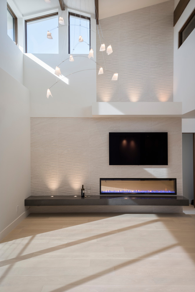Diseño de sala de estar abierta moderna grande con paredes blancas, suelo de madera clara, chimeneas suspendidas, marco de chimenea de baldosas y/o azulejos y televisor colgado en la pared