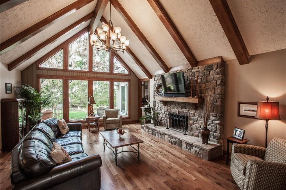 This is an example of a medium sized classic open plan games room in Indianapolis with beige walls, medium hardwood flooring, a standard fireplace, a stone fireplace surround, a wall mounted tv and brown floors.