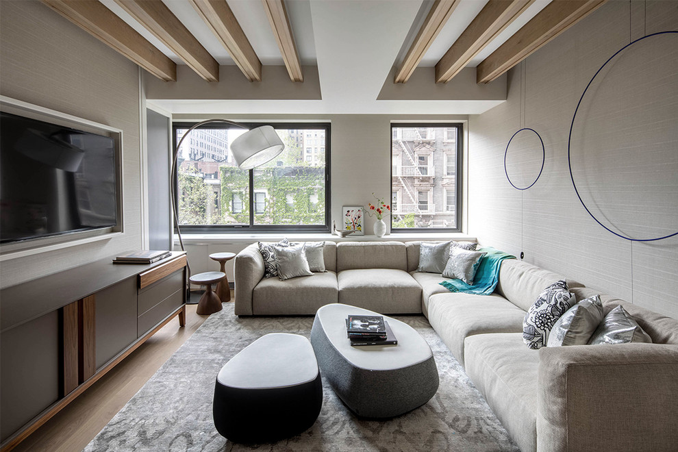 Diseño de sala de estar tipo loft actual pequeña con paredes beige, suelo de madera clara y televisor colgado en la pared