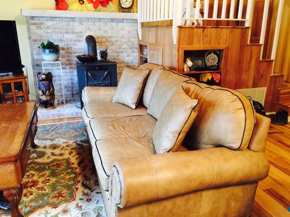 Immagine di un soggiorno chic di medie dimensioni con pareti gialle, pavimento in legno massello medio, cornice del camino in mattoni e porta TV ad angolo