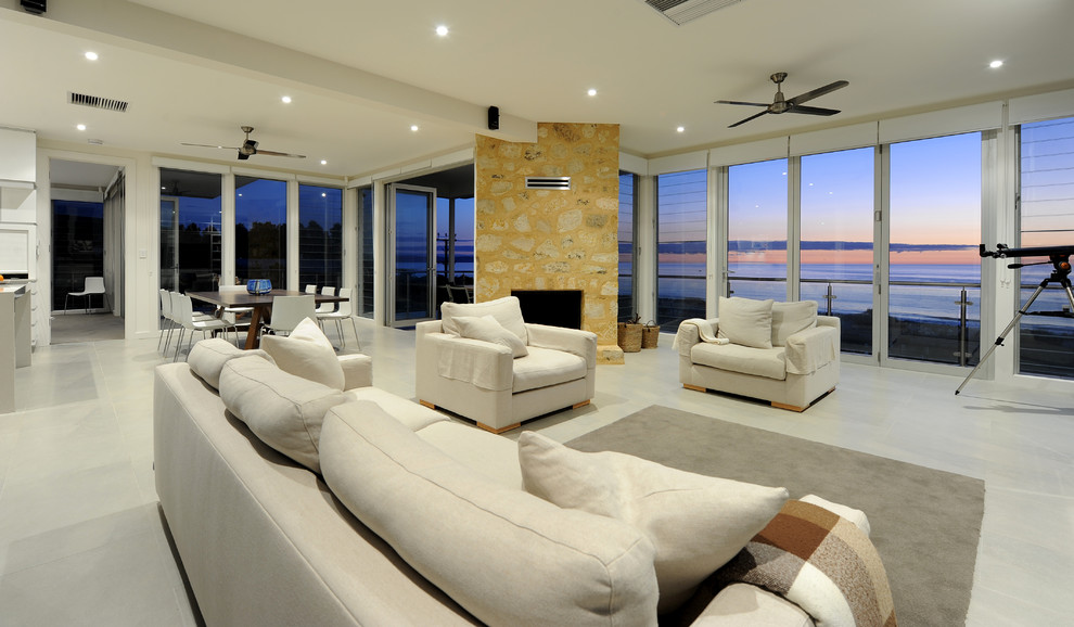 Foto de sala de estar abierta costera extra grande con paredes blancas, suelo de baldosas de cerámica, chimenea de esquina y marco de chimenea de piedra