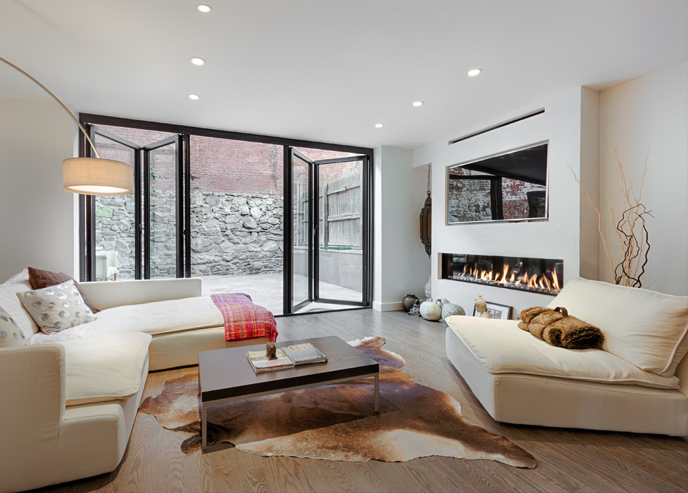 Cette image montre une salle de séjour design avec un mur blanc, un sol en bois brun, une cheminée ribbon et un téléviseur encastré.