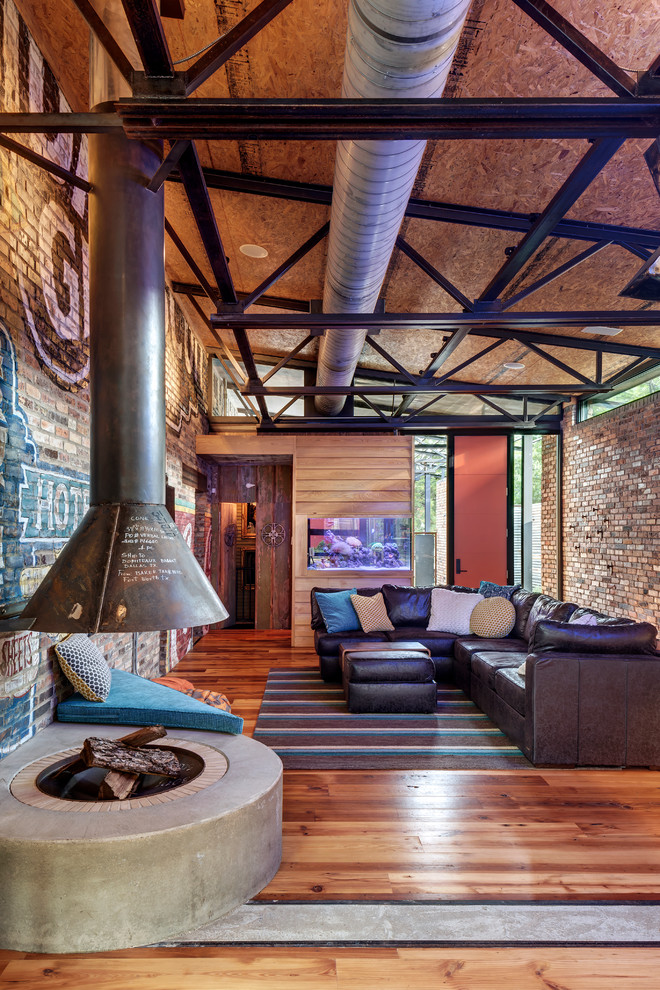 Cette photo montre une salle de séjour industrielle ouverte avec un sol en bois brun et cheminée suspendue.