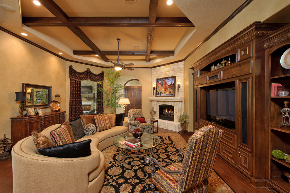 Family room - mediterranean medium tone wood floor family room idea in Houston with beige walls, a standard fireplace, a stone fireplace and a media wall