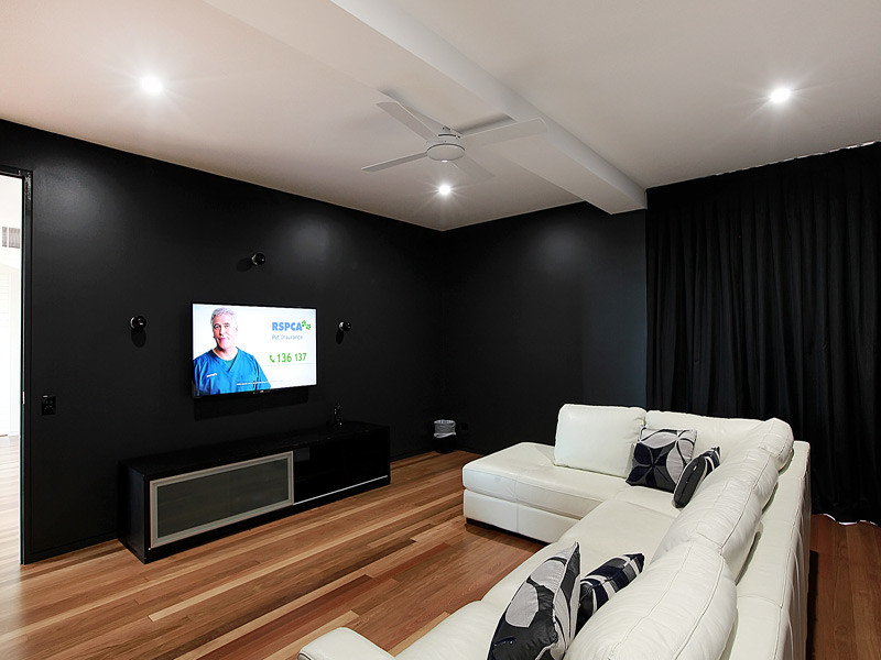Пример оригинального дизайна: изолированный домашний кинотеатр среднего размера в современном стиле с черными стенами, паркетным полом среднего тона и телевизором на стене