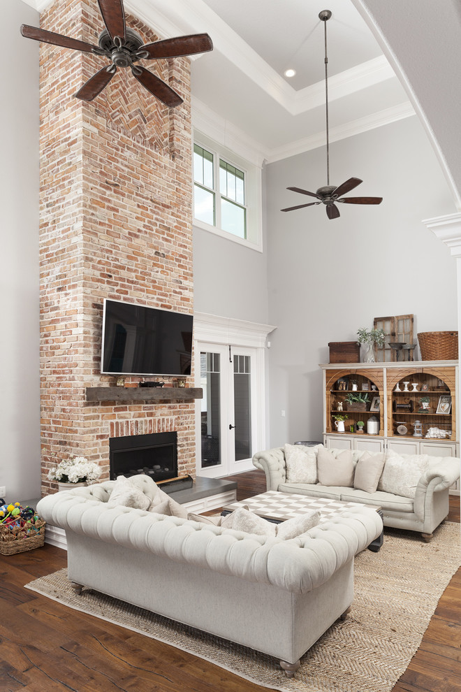 Idée de décoration pour une grande salle de séjour chalet avec un sol en bois brun, une cheminée standard, un manteau de cheminée en brique, un téléviseur fixé au mur et un sol marron.