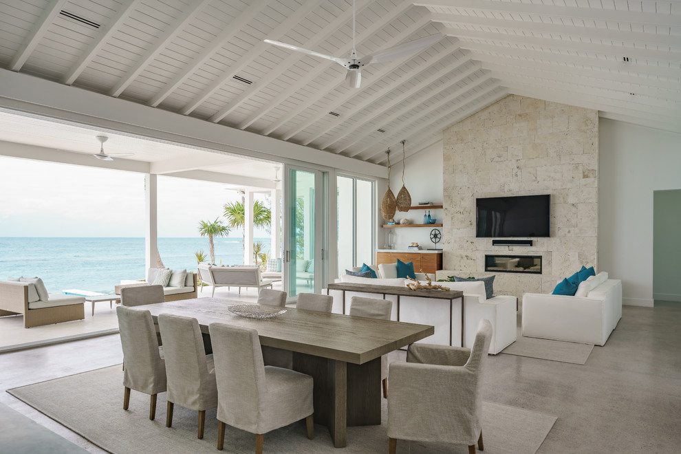 マイアミにあるラグジュアリーな広いビーチスタイルのおしゃれなオープンリビング (ホームバー、白い壁、コンクリートの床、標準型暖炉、石材の暖炉まわり、壁掛け型テレビ、グレーの床) の写真