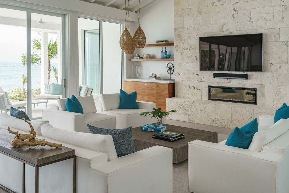 Imagen de sala de estar marinera grande con paredes blancas, suelo de cemento, marco de chimenea de piedra, televisor colgado en la pared, suelo gris y chimenea lineal