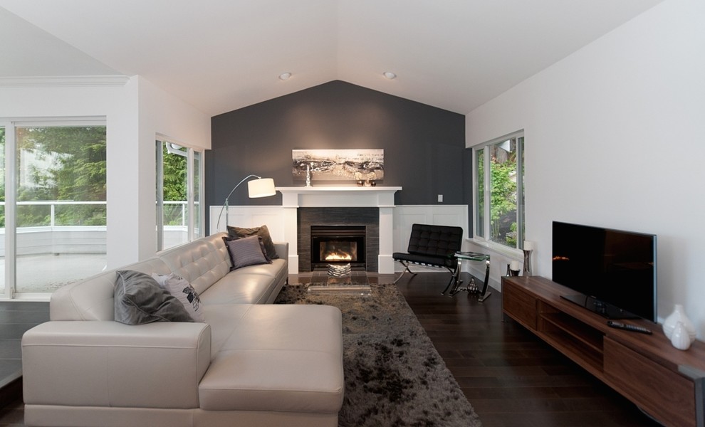 Mittelgroßes, Offenes Modernes Wohnzimmer mit weißer Wandfarbe, dunklem Holzboden, Kamin, Kaminumrandung aus Stein und freistehendem TV in Vancouver