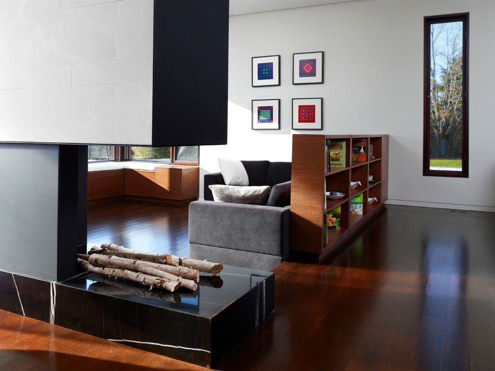 Foto de sala de estar actual con paredes blancas, suelo de madera oscura, chimenea de doble cara, marco de chimenea de piedra y suelo marrón