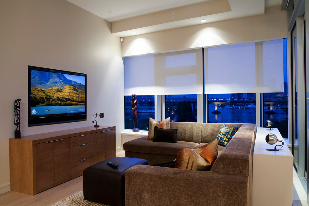 На фото: гостиная комната в современном стиле с бежевыми стенами, телевизором на стене и коричневым диваном с