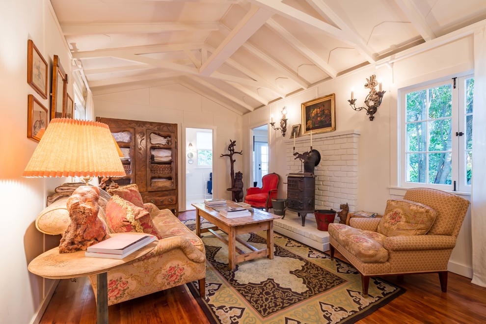 Imagen de sala de estar cerrada de estilo de casa de campo pequeña con paredes blancas, suelo de madera en tonos medios y todas las chimeneas