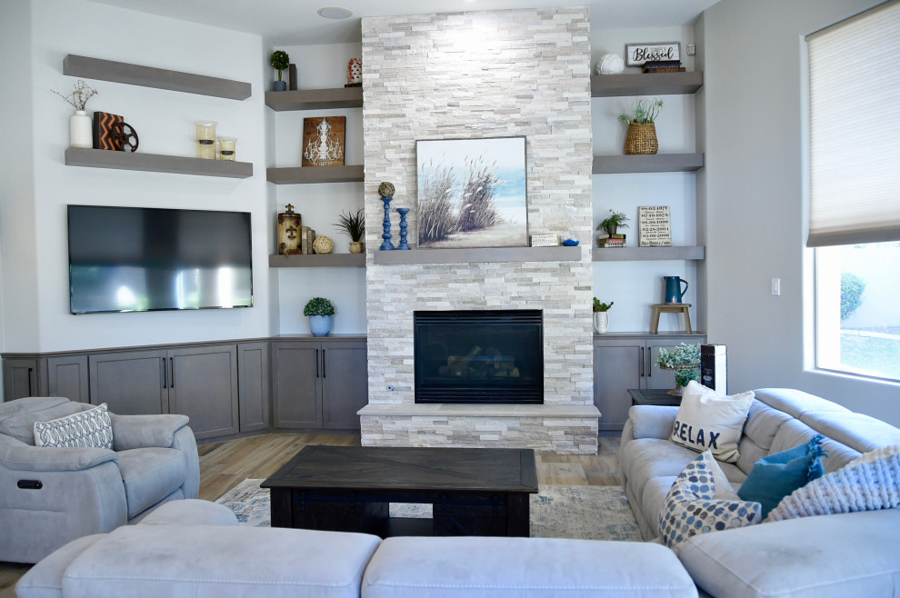 На фото: открытая гостиная комната среднего размера в стиле неоклассика (современная классика) с серыми стенами, полом из керамогранита, стандартным камином, фасадом камина из каменной кладки, телевизором на стене и бежевым полом с
