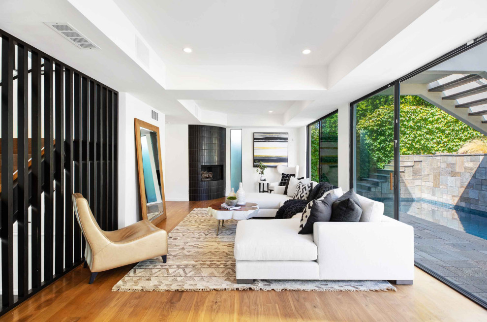 Diseño de sala de estar tipo loft contemporánea de tamaño medio sin televisor con paredes blancas, suelo de madera en tonos medios, chimenea de esquina, marco de chimenea de baldosas y/o azulejos y suelo marrón