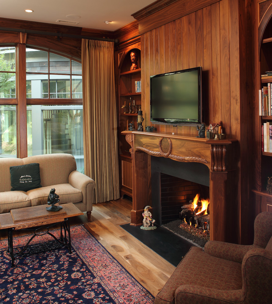 Exempel på ett klassiskt avskilt allrum, med bruna väggar, mellanmörkt trägolv, en standard öppen spis, en spiselkrans i trä och en väggmonterad TV