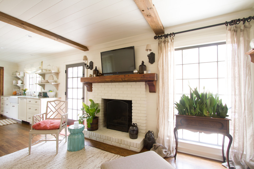 Aménagement d'une salle de séjour classique ouverte avec un mur beige, un sol en bois brun, une cheminée standard, un manteau de cheminée en brique et un téléviseur fixé au mur.