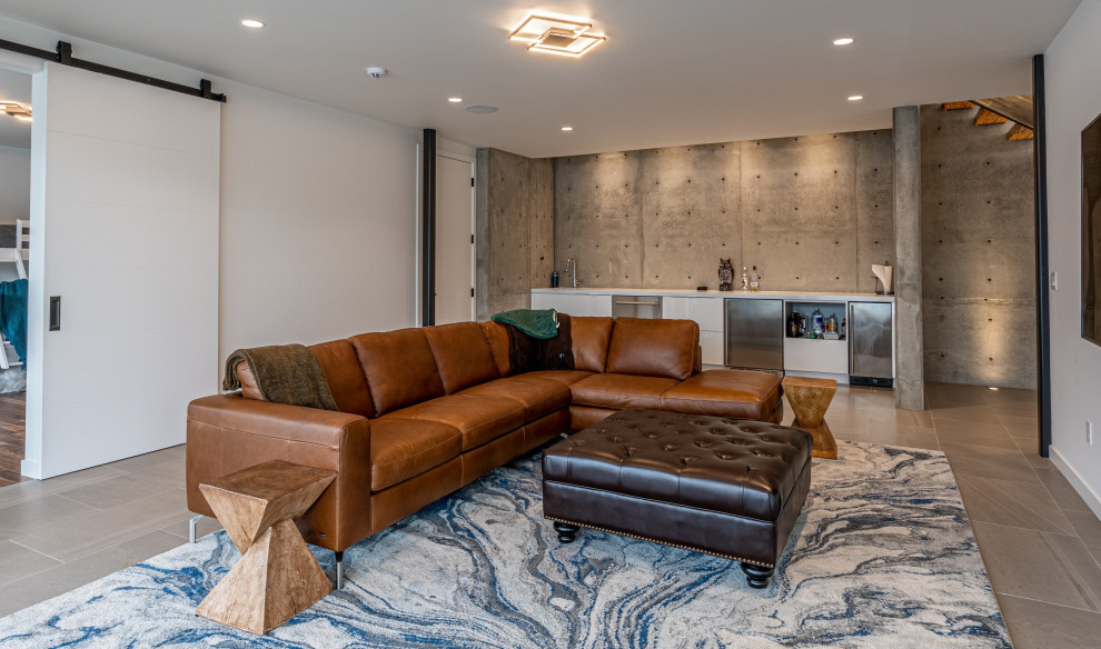 Ejemplo de sala de estar con barra de bar abierta moderna grande con paredes blancas, suelo de baldosas de porcelana, televisor colgado en la pared y suelo beige