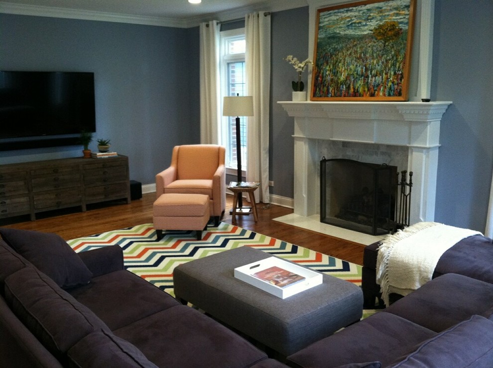 Imagen de sala de estar abierta ecléctica grande con paredes azules, suelo de madera en tonos medios, todas las chimeneas, marco de chimenea de yeso y televisor colgado en la pared