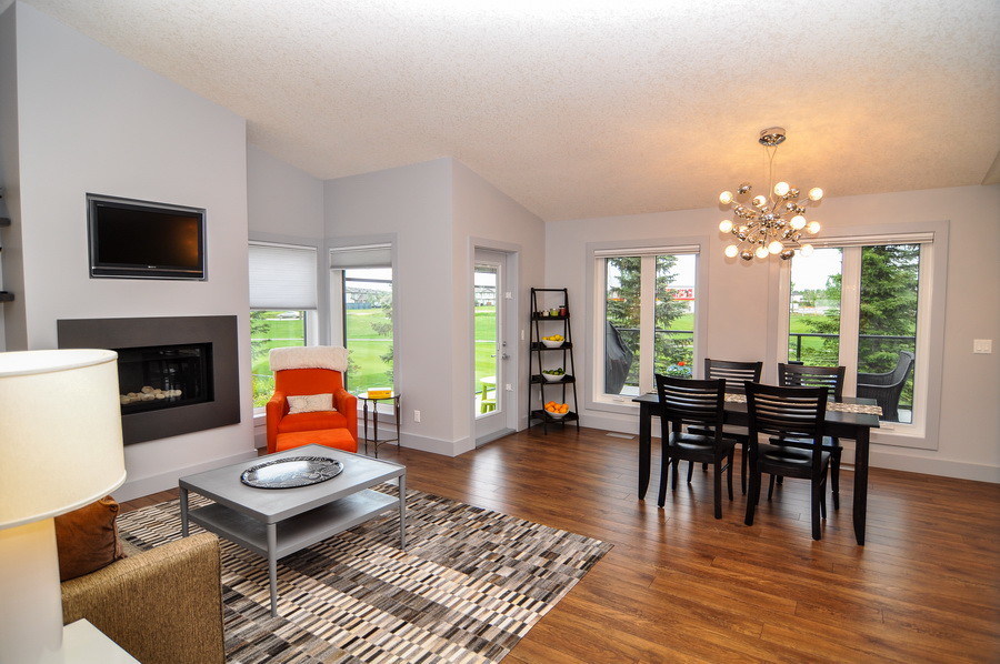 Mittelgroßes, Offenes Klassisches Wohnzimmer mit grauer Wandfarbe, braunem Holzboden, Kamin, gefliester Kaminumrandung, TV-Wand und braunem Boden in Calgary