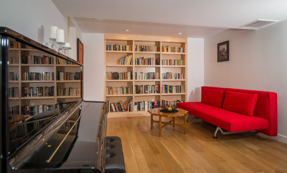 Cette photo montre une salle de séjour mansardée ou avec mezzanine rétro de taille moyenne avec une bibliothèque ou un coin lecture, un mur blanc, un sol en bois brun, aucune cheminée et un téléviseur indépendant.