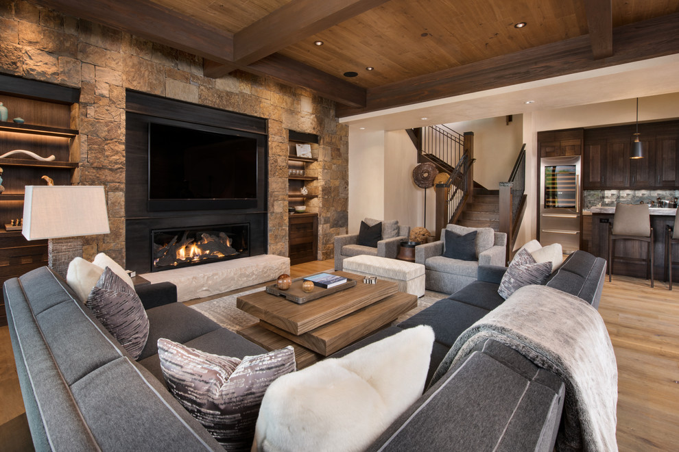 Photo of an expansive rustic open plan games room in Denver with beige walls, light hardwood flooring, a metal fireplace surround, a wall mounted tv, a home bar, a ribbon fireplace and feature lighting.