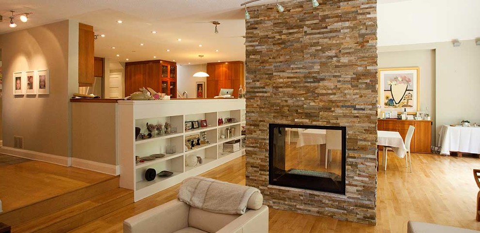 Photo of a medium sized traditional open plan games room in Ottawa with beige walls, light hardwood flooring, a two-sided fireplace, a stone fireplace surround, no tv and brown floors.