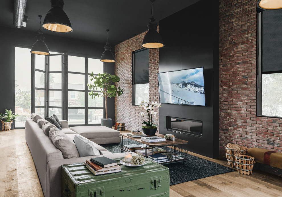 Imagen de sala de estar abierta industrial grande con paredes negras, televisor colgado en la pared, chimenea lineal, marco de chimenea de metal, suelo laminado y alfombra