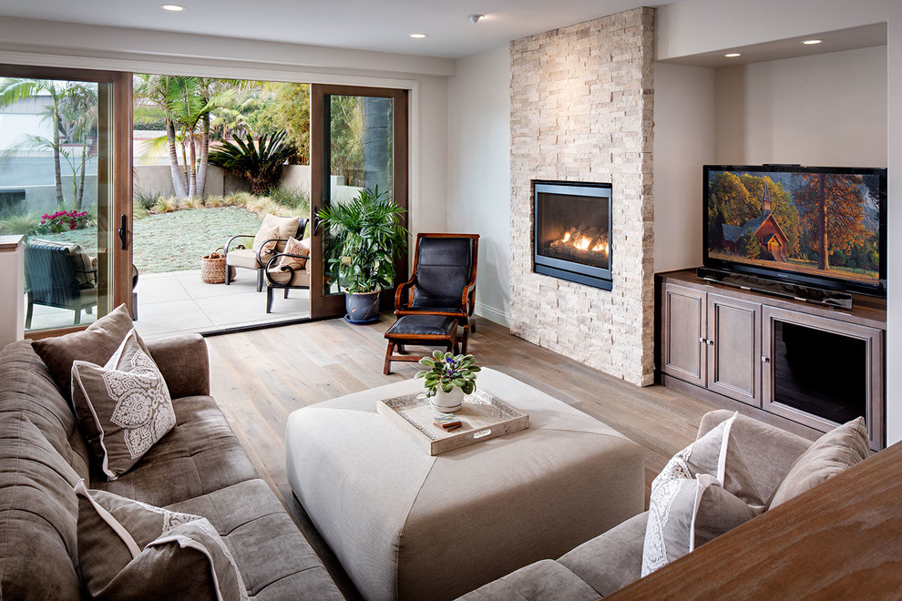 Großes Mediterranes Wohnzimmer mit weißer Wandfarbe, braunem Holzboden, Kamin, Kaminumrandung aus Stein und TV-Wand in San Diego