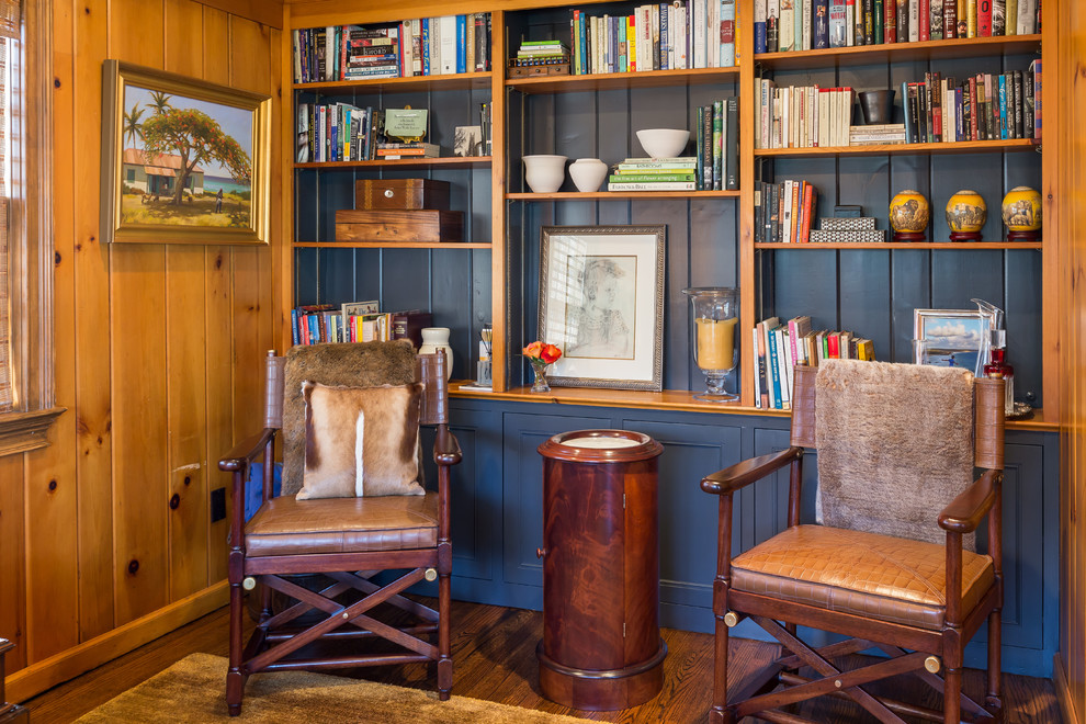 Imagen de sala de estar con biblioteca cerrada rústica pequeña sin chimenea con paredes azules, suelo de madera en tonos medios, pared multimedia y suelo marrón