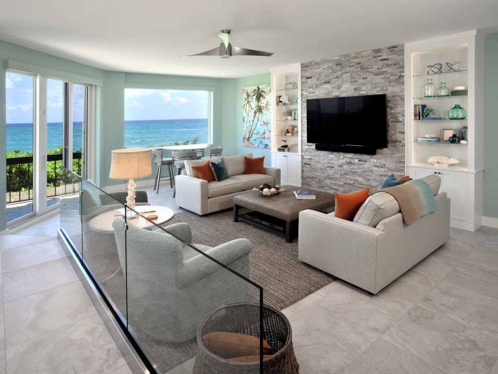 Modelo de sala de estar abierta costera de tamaño medio con paredes azules, suelo de baldosas de porcelana, televisor colgado en la pared y suelo gris